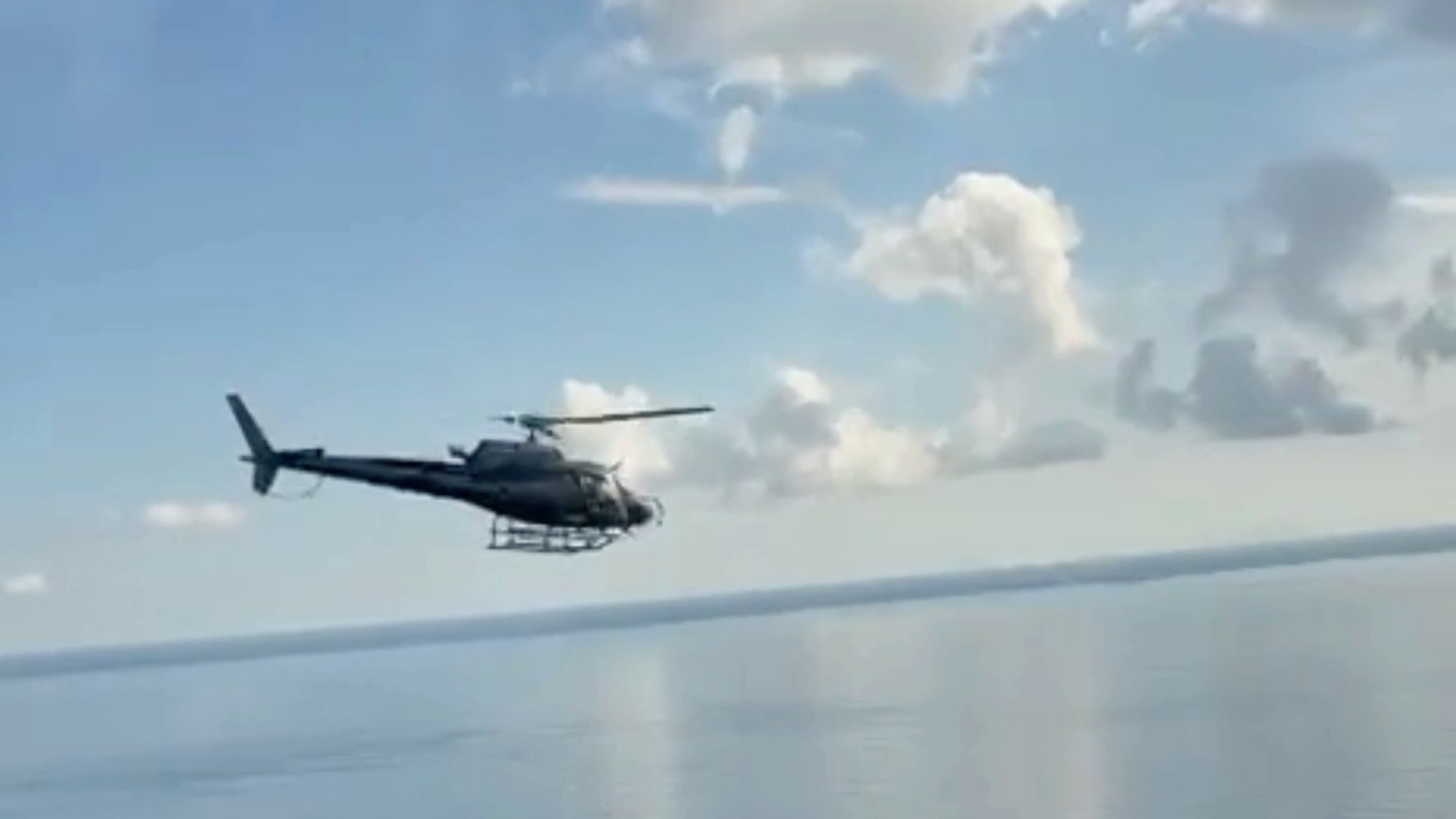 Un hélicoptère en vol au-dessus de la mer, sous un ciel nuageux.